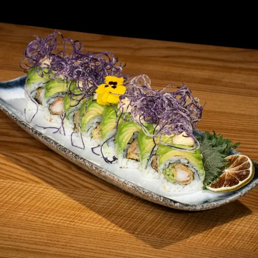 Dragon roll cu avocado si flori comestibile, pe un platou lung de ceramica