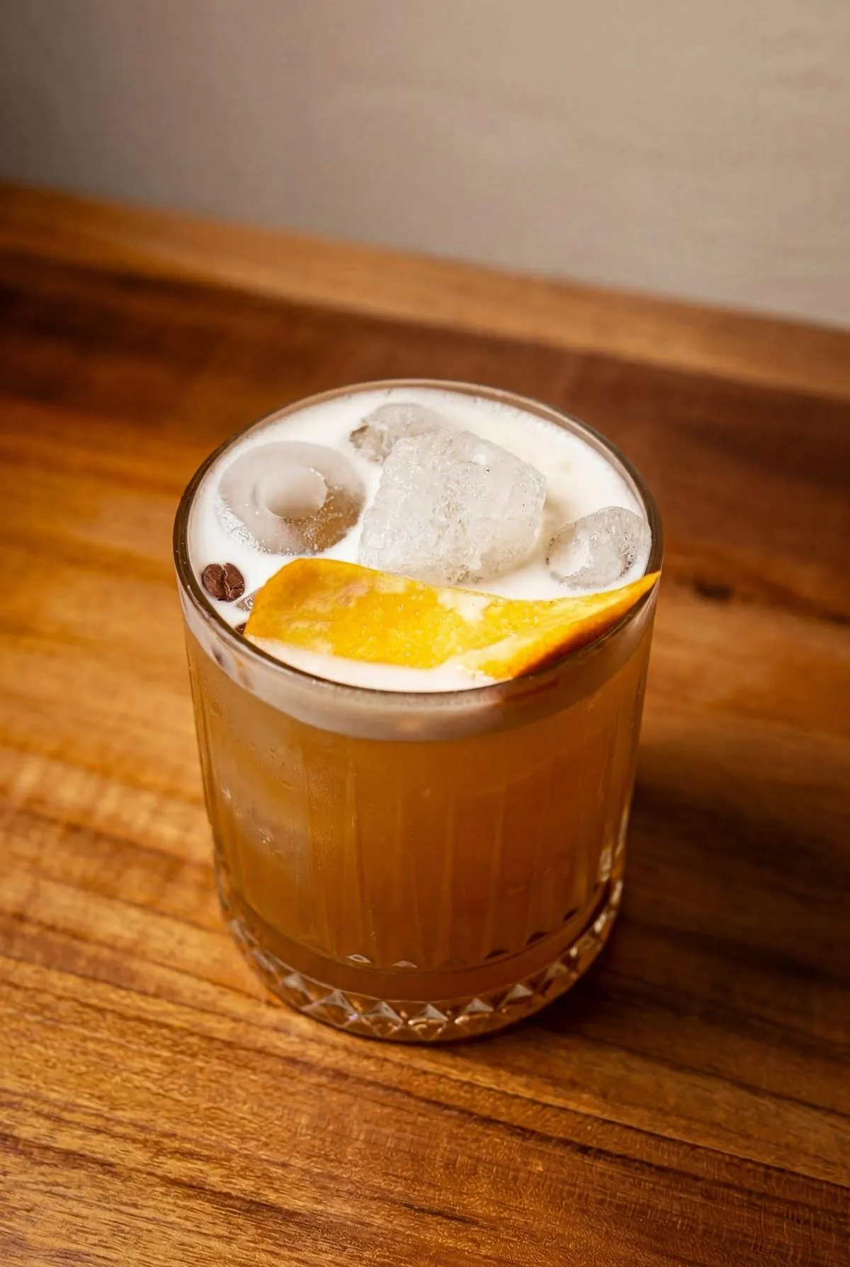 Cocktail semnatura chihlimbar cu coaja de portocala pe masa de lemn