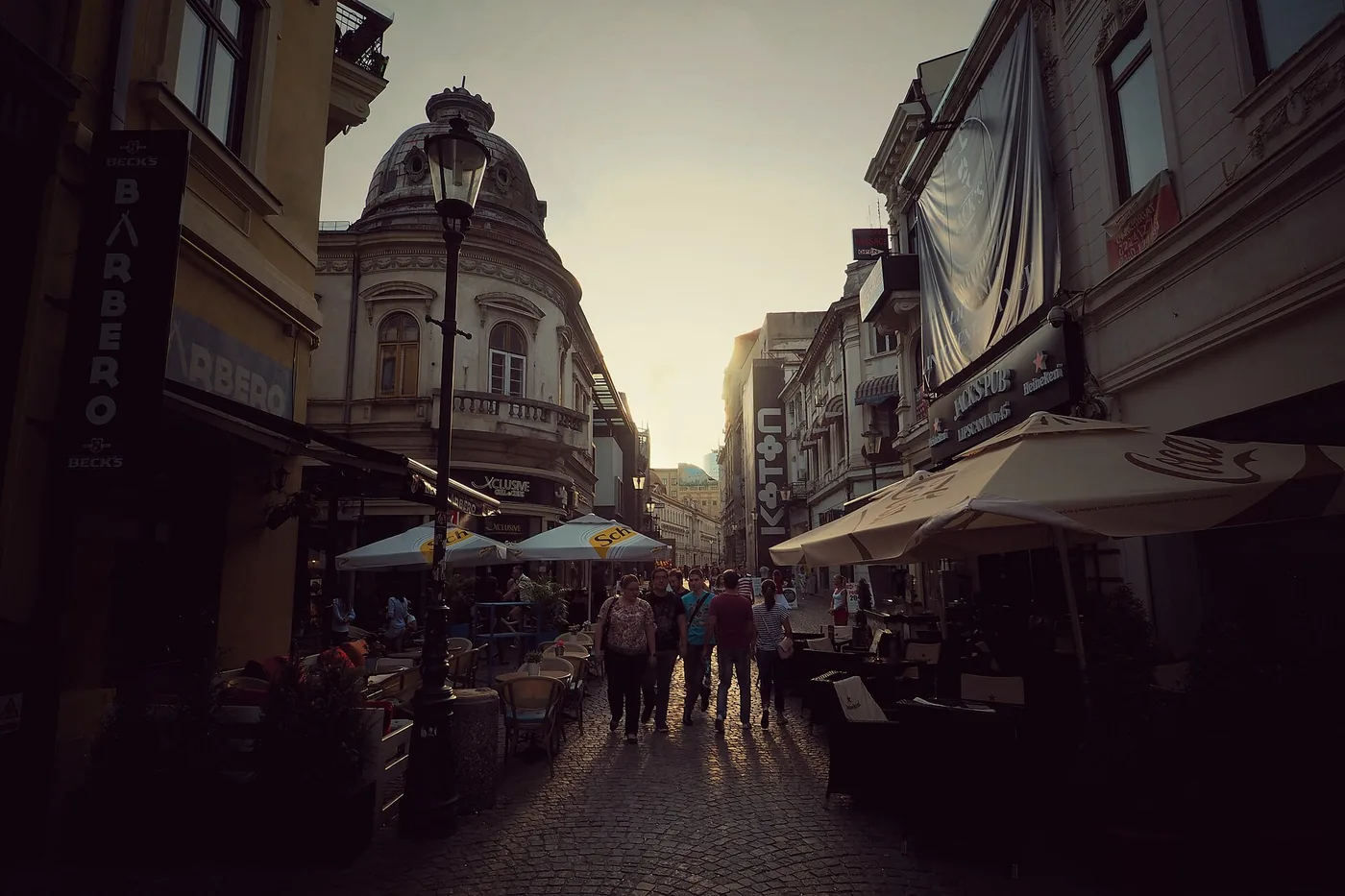 Strada Lipscani din București la apus, cu umbrele de terasă pe ambele părți și oameni pe pavaj
