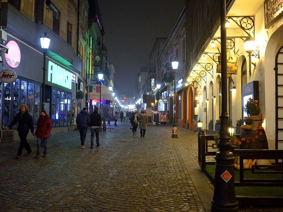Oameni în paltoane pe o stradă pietruită din Centrul Vechi, noaptea
